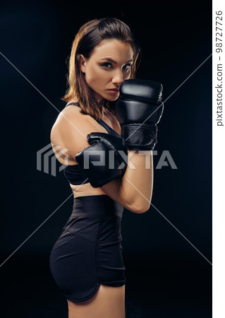 Athletic woman in boxing gloves is practicing karate in studio. Athletic woman in boxing gloves is practicing karate in studio. 98727726