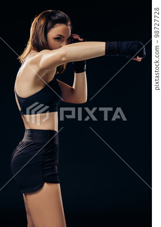 Athletic woman in boxing mittens is practicing karate in studio. Athletic woman in boxing mittens is practicing karate in studio. 98727728