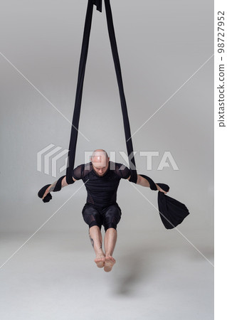 Athletic man in a black sport suit is performing an acrobatic elements in a studio. Athletic man in a black sport suit is performing an acrobatic elements in a studio. 98727952