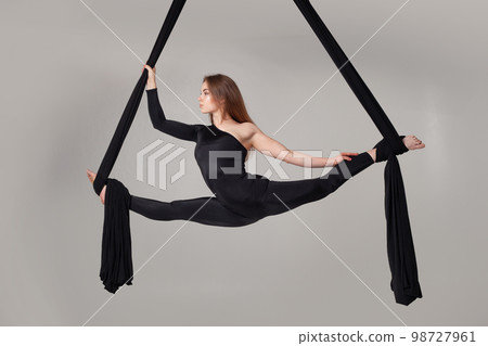 Beautiful girl in a black sport suit is performing an acrobatic elements in a studio. Beautiful girl in a black sport suit is performing an acrobatic elements in a studio. 98727961
