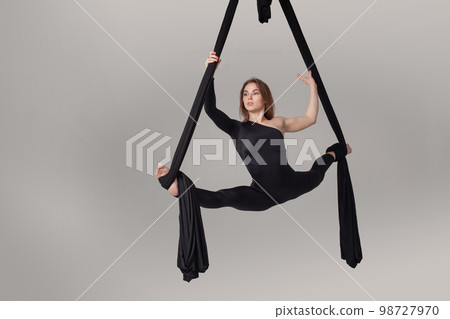 Beautiful girl in a black sport suit is performing an acrobatic elements in a studio. Beautiful girl in a black sport suit is performing an acrobatic elements in a studio. 98727970