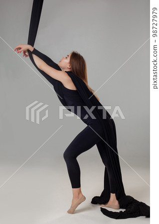 Beautiful girl in a black sport suit is performing an acrobatic elements in a studio. Beautiful girl in a black sport suit is performing an acrobatic elements in a studio. 98727979