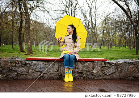 Coping with stress and anxiety. Practicing mindfulness and relaxation techniques. Happy senior woman in yellow rain coat with yellow umbrella walking and enjoying life in rainy park Coping with stress and anxiety. Practicing mindfulness and relaxation techniques. Happy senior woman in yellow rain coat with yellow umbrella walking and enjoying life in rainy park 98727986