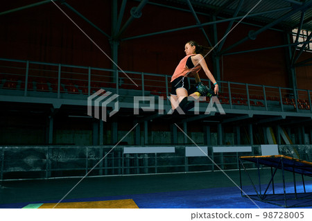 Rollerblader jump high from big air ramp performing trick. Indoors skate park equipment. 98728005