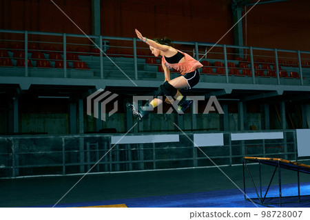 Rollerblader jump high from big air ramp performing trick. Indoors skate park equipment. 98728007