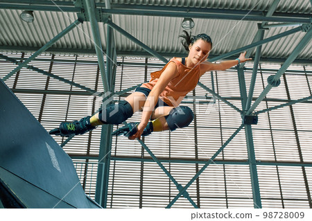 Rollerblader jump high from big air ramp performing trick. Indoors skate park equipment. Rollerblader jump high from big air ramp performing trick. Indoors skate park equipment. 98728009
