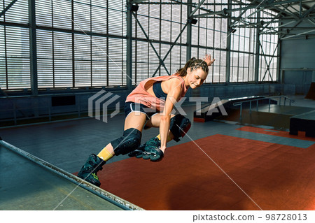 Rollerblader jump high from big air ramp performing trick. Indoors skate park equipment. 98728013