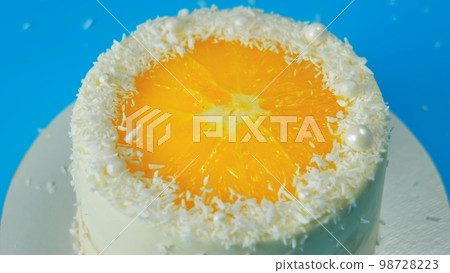 Cake with orange and coconut shavings spinning on a blue background. 98728223
