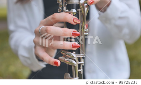 A girl plays the clarinet in the summer in the park. Close-up of her hands. A girl plays the clarinet in the summer in the park. Close-up of her hands. 98728233