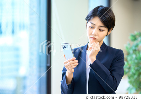 穿著西裝的中層女商人在辦公室操作智能手機 穿著西裝的中層女商人在辦公室操作智能手機 98728313