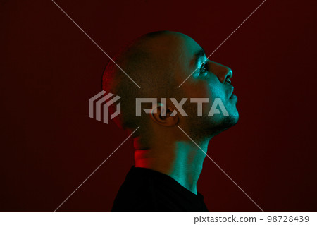 Studio shot of a young tattoed bald man posing against a red background. 90s style. Studio shot of a young tattoed bald man posing against a red background. 90s style. 98728439