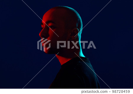 Studio shot of a young tattoed bald man posing against a blue background. 90s style. 98728459