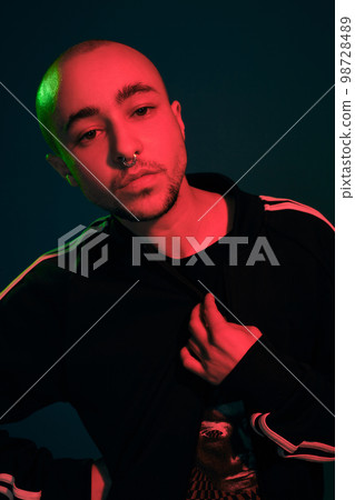 Studio shot of a young tattoed bald man posing against a colorful background. 90s style. 98728489