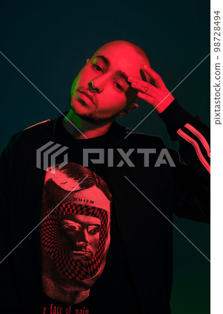 Studio shot of a young tattoed bald man posing against a colorful background. 90s style. Studio shot of a young tattoed bald man posing against a colorful background. 90s style. 98728494