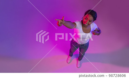 Cheerful Black Woman Standing In Neon Light And Pointing At Copy Space Cheerful Black Woman Standing In Neon Light And Pointing At Copy Space 98728606