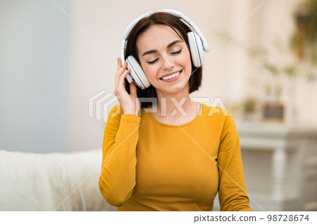 Joyful young woman listening to music, using wireless headphones 98728674