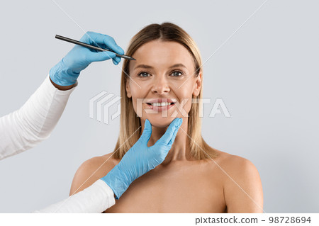Beauty clinic patient ready for face lifting, doctor using marker Beauty clinic patient ready for face lifting, doctor using marker 98728694