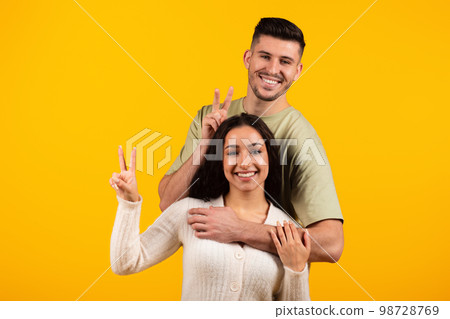 Smiling young arabic couple in casual hugging, showing peace sign with fingers and make horns, have fun Smiling young arabic couple in casual hugging, showing peace sign with fingers and make horns, have fun 98728769