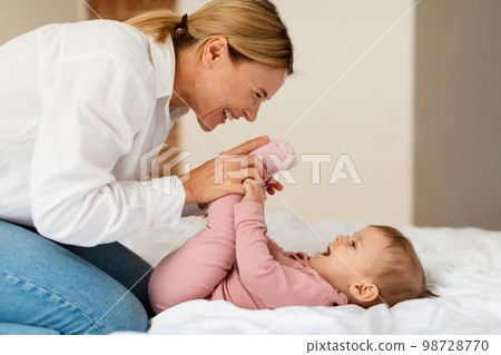 Child care. Happy woman making gymnastics to her baby girl, playing and bonding with infant, enjoying time together Child care. Happy woman making gymnastics to her baby girl, playing and bonding with infant, enjoying time together 98728770