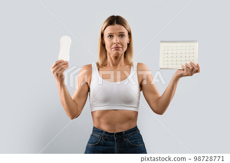 Unhappy middle aged woman demonstrates periods calendar and sanitary napkin Unhappy middle aged woman demonstrates periods calendar and sanitary napkin 98728771