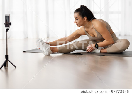 Young woman yoga instructor broadcasting while strecthing at home Young woman yoga instructor broadcasting while strecthing at home 98728996