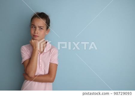 Little emotional teenage girl in pink shirt 11, 12 years old on an isolated blue background. Children's studio portrait. Place text to copy space for caption, advertising children's goods. Little emotional teenage girl in pink shirt 11, 12 years old on an isolated blue background. Children's studio portrait. Place text to copy space for caption, advertising children's goods. 98729093