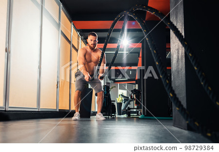 Athletic caucasian young man with battle rope doing exercise in fitness gym. Keeping fit with cross training 98729384