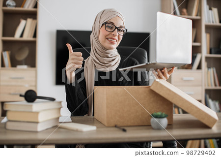 Muslim woman doing live stream while unpacking box with new laptop. 98729402