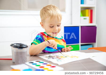 Cute boy drawing picture by using watercolors indoors. Cute boy drawing picture by using watercolors indoors. 98729456