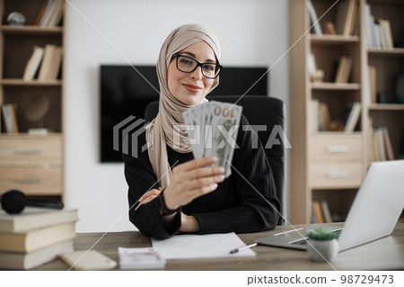 Portrait of happy young attractive muslim female accountant holding cash banknotes 98729473
