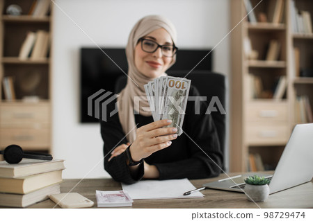 Focus on hands of happy young attractive muslim female accountant holding cash banknotes Focus on hands of happy young attractive muslim female accountant holding cash banknotes 98729474
