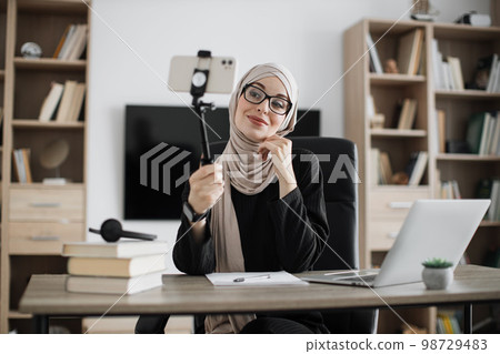 Close up portrait of young muslim woman in hijab taking selfie on her smart phone using stick Close up portrait of young muslim woman in hijab taking selfie on her smart phone using stick 98729483