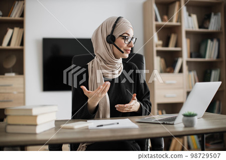 Young woman in headset having video call with partners, working process at office. Young woman in headset having video call with partners, working process at office. 98729507