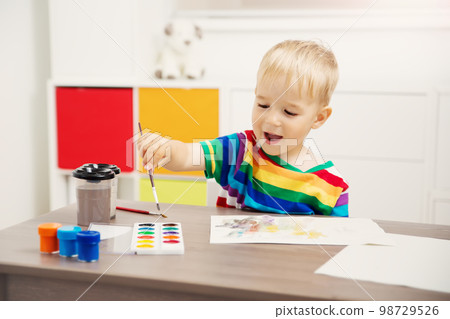 Cute boy drawing picture by using watercolors and couache indoors. Cute boy drawing picture by using watercolors and couache indoors. 98729526