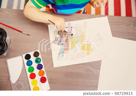 Little child drawing picture by using watercolors indoors. 98729915