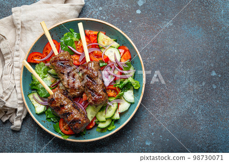Grilled skewer meat beef kebabs on sticks served with fresh vegetables salad on plate on rustic concrete background from above. Traditional Middle Eastern Turkish dish Kebab, space for text 98730071