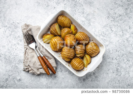 Hasselback baked potatoes in white ceramic casserole dish on white concrete table background Hasselback baked potatoes in white ceramic casserole dish on white concrete table background 98730086