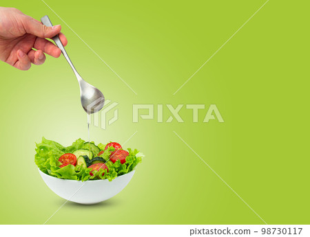 Bowl of salad and male hand pouring oil with spoon over salad isolated 98730117