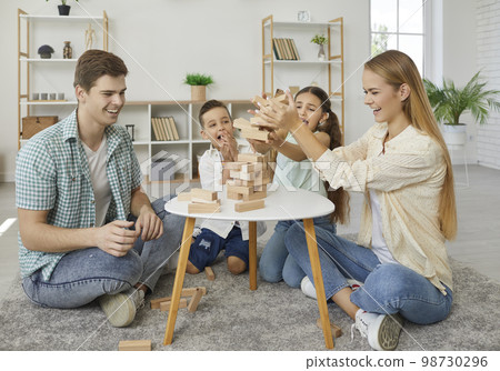 Friendly family with two children are playing tumbling tower sitting on floor at home. Friendly family with two children are playing tumbling tower sitting on floor at home. 98730296