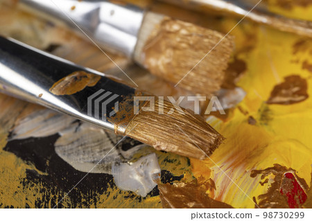 Artistic brushes while painting on canvas with gold paints Artistic brushes while painting on canvas with gold paints 98730299