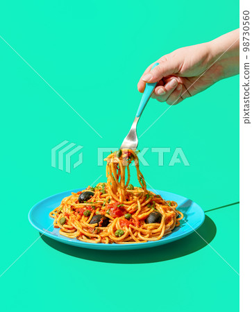 Eating spaghetti puttanesca, a vegan pasta dish, minimalist on a green background 98730560