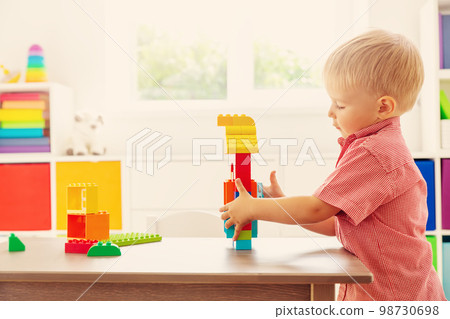 Cute child sitting at the table and playing with constructor. Cute child sitting at the table and playing with constructor. 98730698