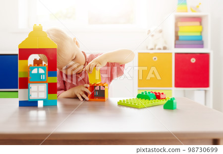Cute child sitting at the table and playing with constructor. Cute child sitting at the table and playing with constructor. 98730699