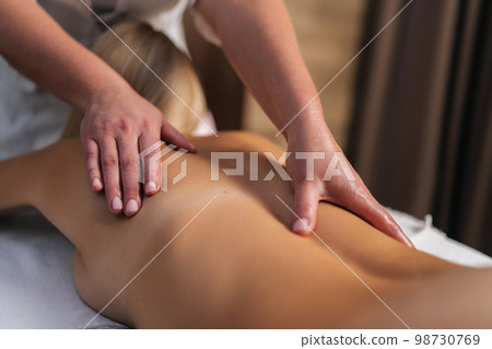 Cropped shot of unrecognizable male masseur doing back and shoulder massage to female client with beautiful skin lying in spa salon. Male masseur professionally massaging young woman client. Cropped shot of unrecognizable male masseur doing back and shoulder massage to female client with beautiful skin lying in spa salon. Male masseur professionally massaging young woman client. 98730769