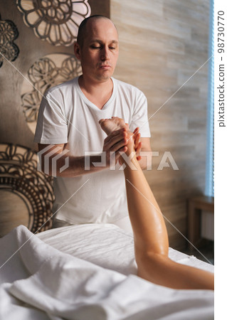 Vertical portrait of professional male masseur massaging heel of foot of unrecognizable female client lying on massage table in spa salon. Concept of body care and rehabilitation of spiritual peace. Vertical portrait of professional male masseur massaging heel of foot of unrecognizable female client lying on massage table in spa salon. Concept of body care and rehabilitation of spiritual peace. 98730770