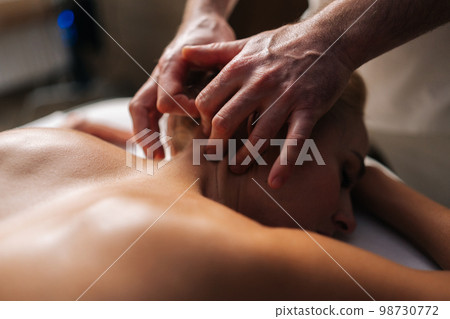 Close up cropped shot of unrecognizable male masseur doing therapeutic neck massage for young woman lying down in spa salon. Relaxed naked female client woman getting relaxing massage. Close up cropped shot of unrecognizable male masseur doing therapeutic neck massage for young woman lying down in spa salon. Relaxed naked female client woman getting relaxing massage. 98730772