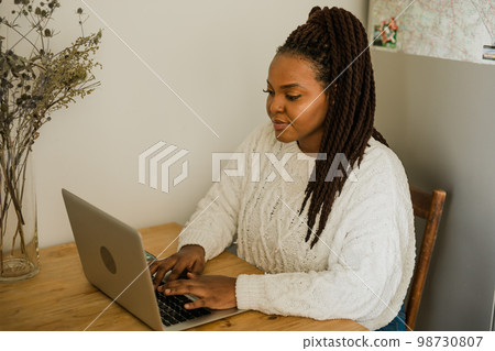 Portrait african american woman using laptop while sitting on chair in living room - student, video call and working at home concept Portrait african american woman using laptop while sitting on chair in living room - student, video call and working at home concept 98730807