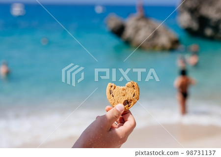 Child is holding a cookie on the beach. Child is holding a cookie on the beach. 98731137