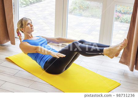 Woman in sportswear is doing exercises on the mat on the floor at home Woman in sportswear is doing exercises on the mat on the floor at home 98731236