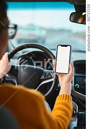 Screen blank mockup mobile phone in the hands of a woman driver in a car Screen blank mockup mobile phone in the hands of a woman driver in a car 98731528